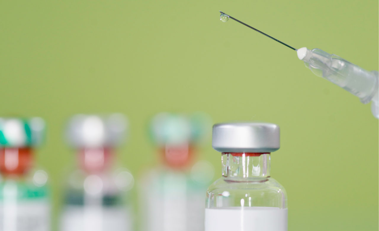 A syringe and vials of medication against a green background