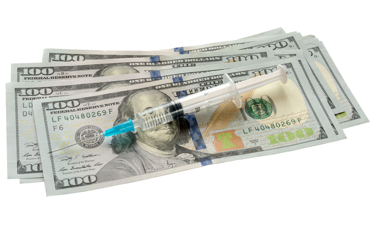 A capped syringe sits atop four US $100 bills